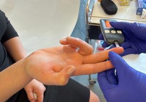 Medicul măsoară glicemia pacientului cu ajutorul unui glucometru, folosind o picătură de sânge prelevată din deget.